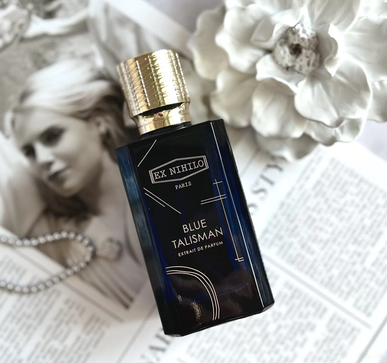 Blue Talisman Extrait bottle against monochrome fashion imagery and flowers