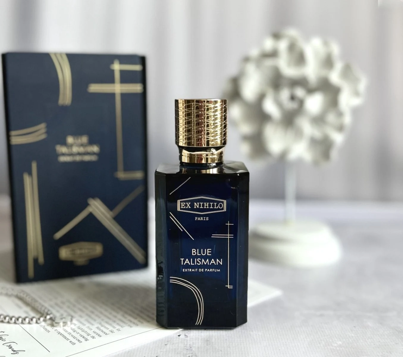 Blue Talisman Extrait bottle in front of its box and white sculpture